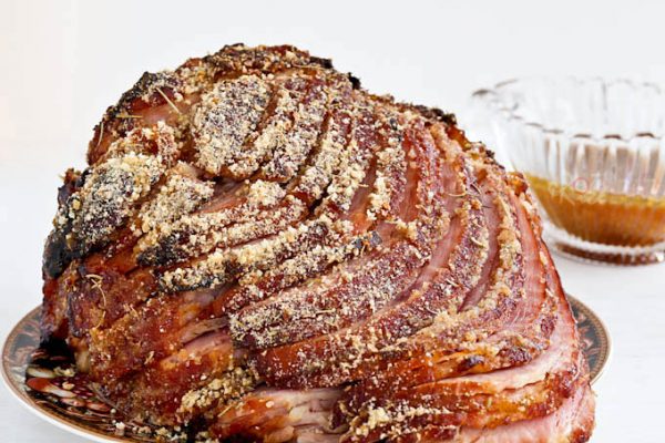 Baked Ham with Marmalade Almond Crust cascading down a plate with remaining marinade used as sauce in a gravy boat.